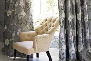An image showing stunning grey curtains with a delicate floral print on them with a yellow armchair in between