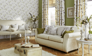 An image showing a well decorated living room with interesting floral curtains, matching wallpaper, roman blinds, soft furnishings and cushions