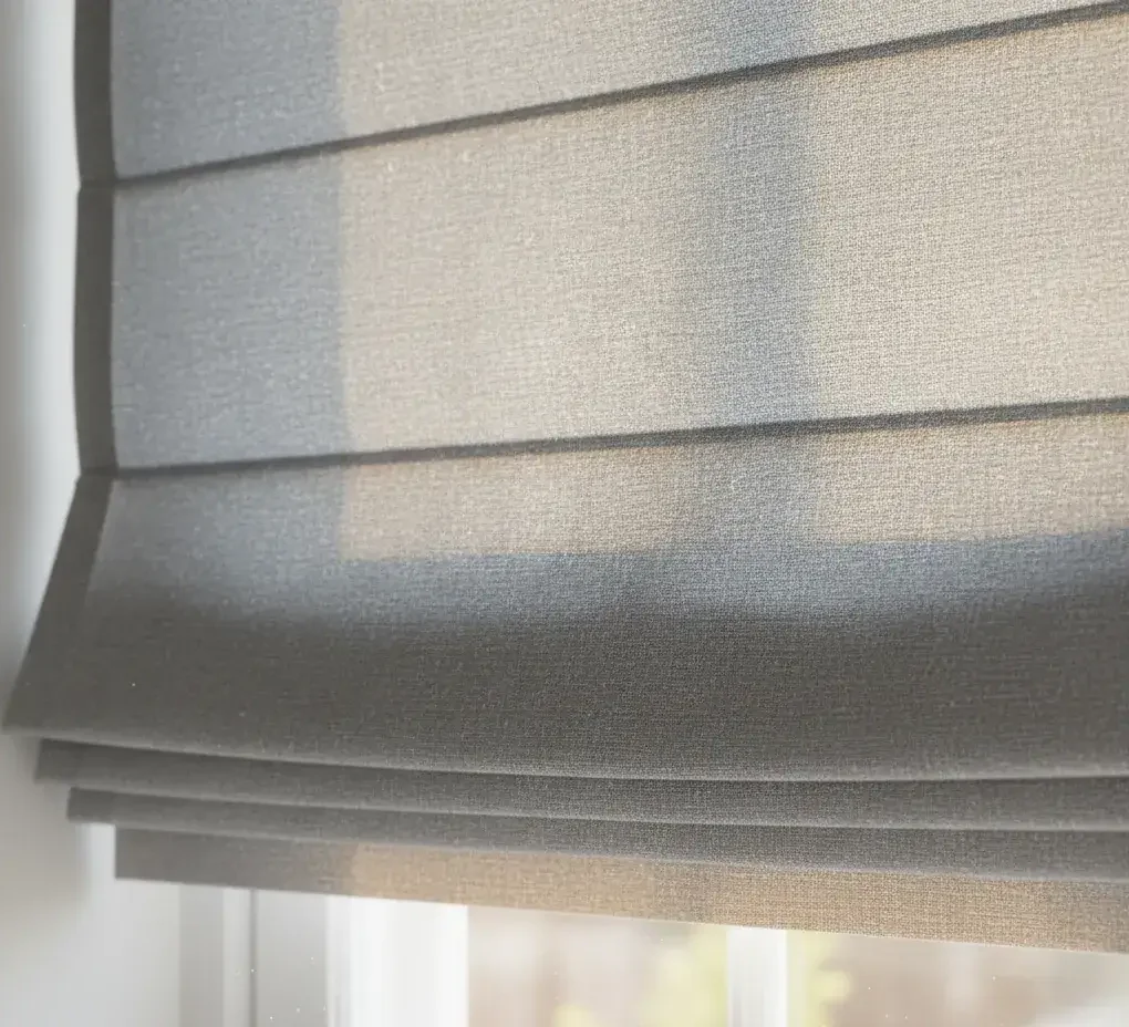 Grey Roman blind covering a window with daylight shining through.